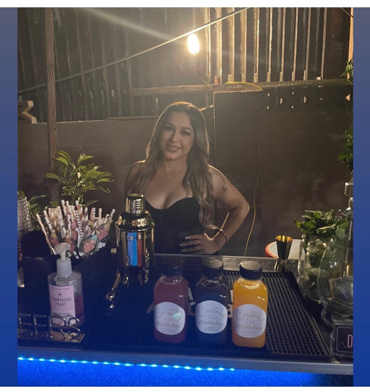 Dolls Bartending bartender smiling behind a birthday bar with custom-labeled juices, a shaker, and fresh garnishes