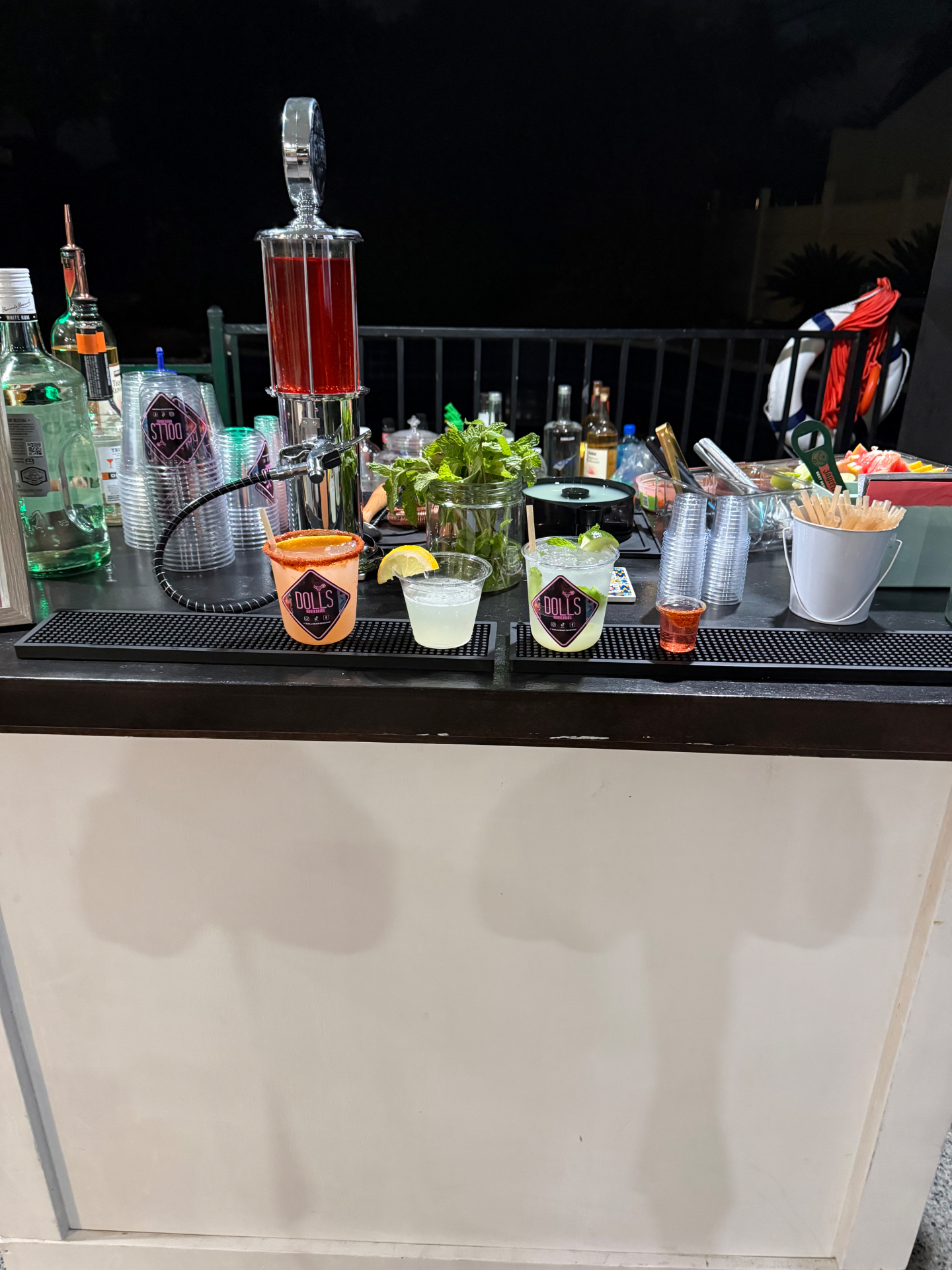 Dolls Bartending night bar setup with a red cocktail dispenser, garnishes, and signature drinks