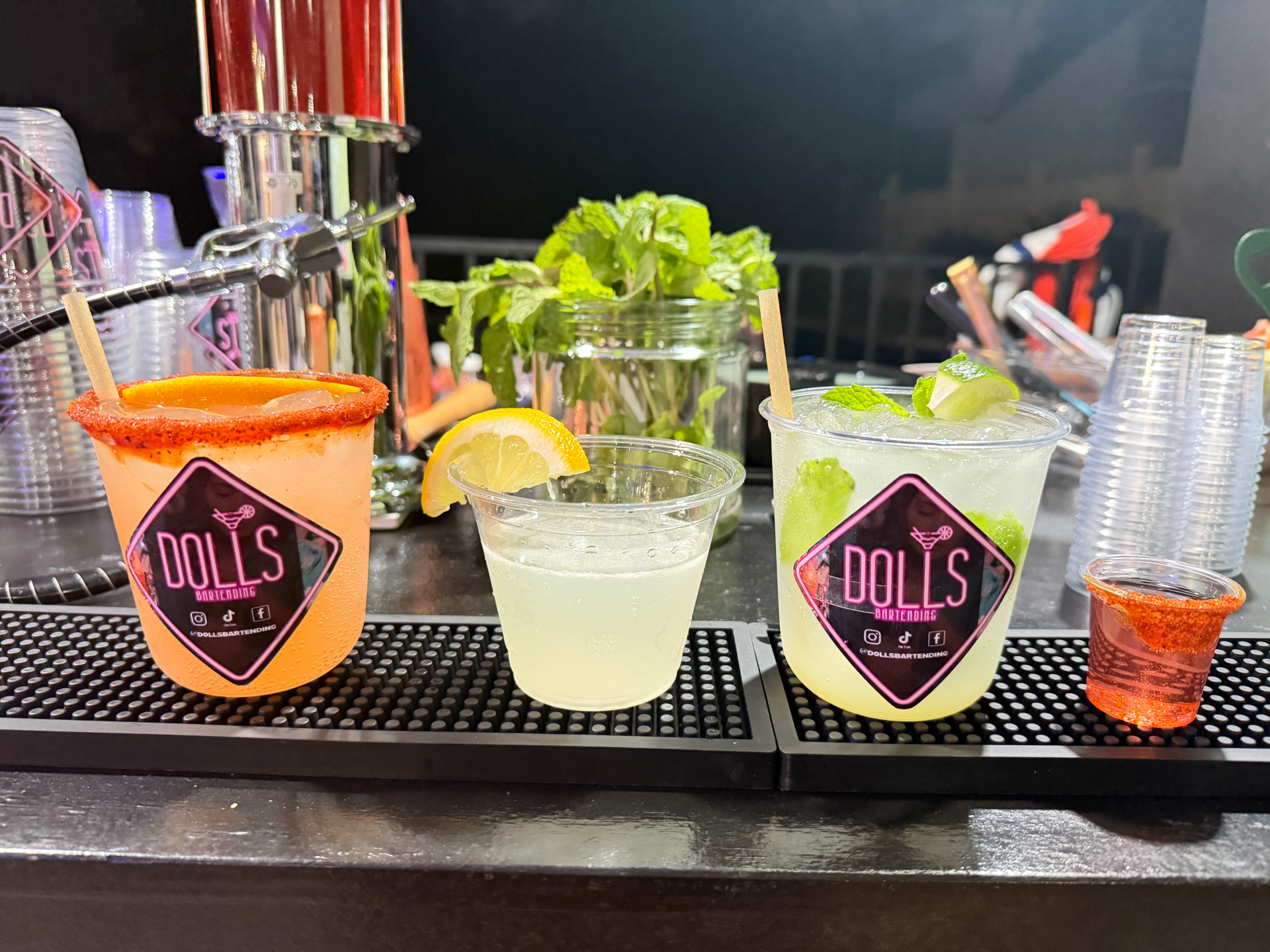 Three signature Dolls Bartending cocktails with fresh orange, lemon, lime, and mint garnishes